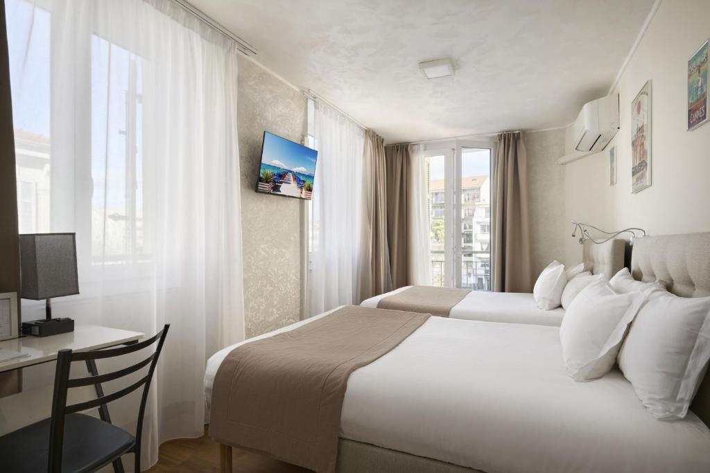 a bedroom with two beds and a desk and a window at Hotel des Congrès et Festivals in Cannes