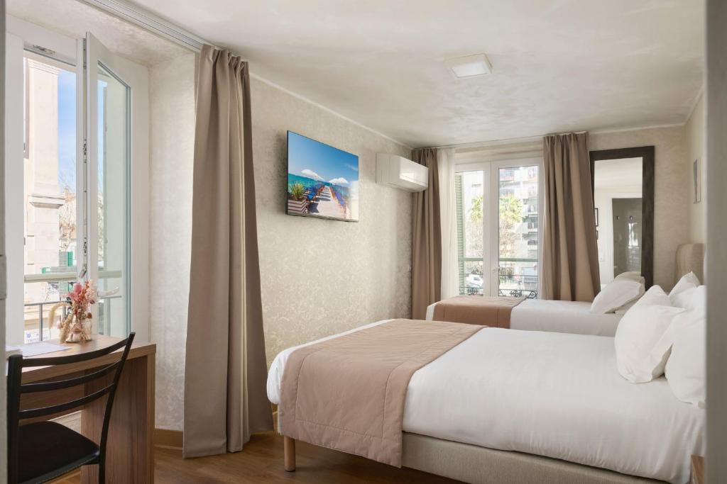 a hotel room with two beds and a desk and windows at Hotel des Congrès et Festivals in Cannes