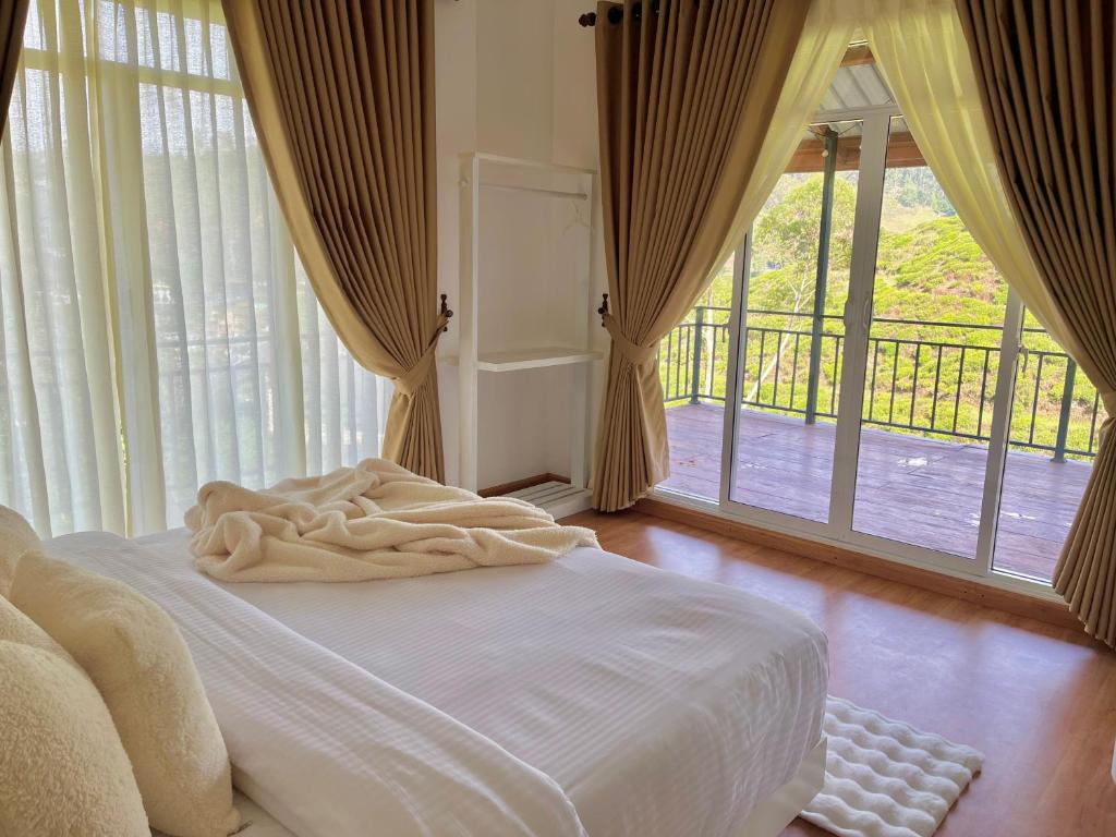 Cama blanca en habitación con ventanas grandes en Seeming Lodge, en Nuwara Eliya