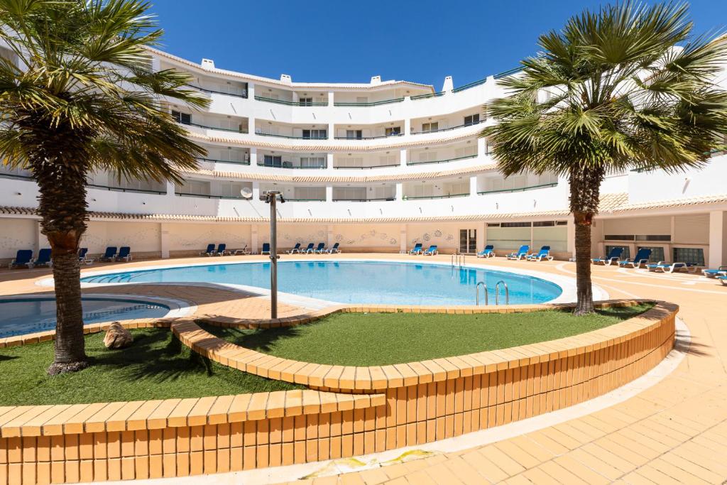 a large building with a swimming pool and palm trees at Apartment Estrelícia Direct beach access in Porches