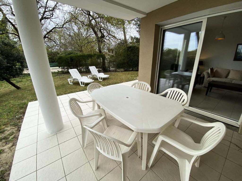 Une table à manger et des chaises blanches sont disponibles sur la terrasse. dans l'établissement Résidence Villa Marine - 021- Bel appartement avec son jardin privatif MAE-1841, à Soulac-sur-Mer