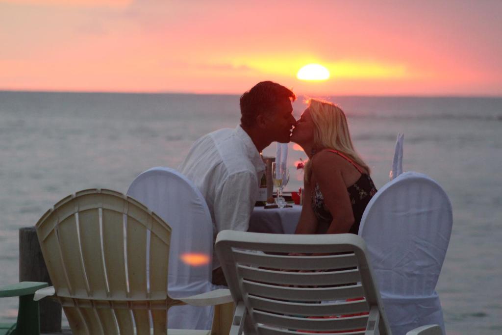 a man and a woman kissing at a table on the beach at Splash Inn Dive Resort & Villas in West End