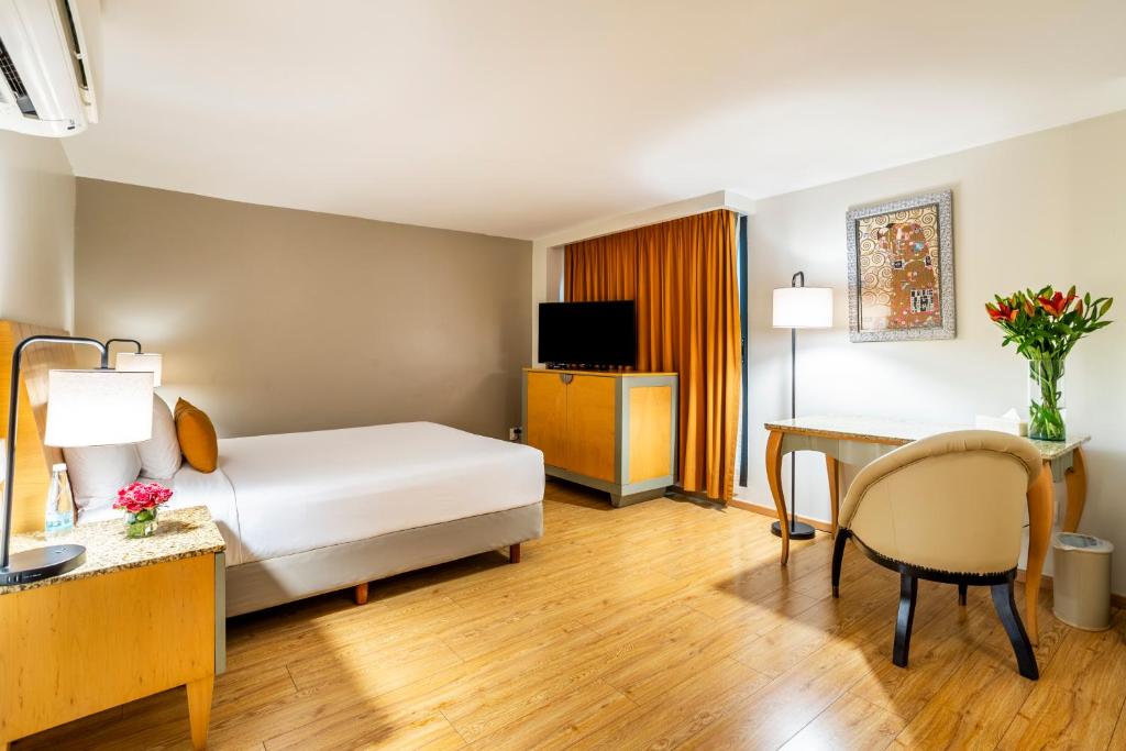 A warm-toned bedroom includes a television, desk and small seating area.