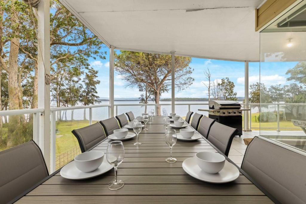 a long table with chairs and wine glasses on a balcony at Island Point by Experience Jervis Bay in St Georges Basin
