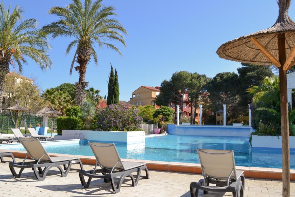 a pool with chairs and an umbrella and palm trees at Malibu Village in Canet-en-Roussillon