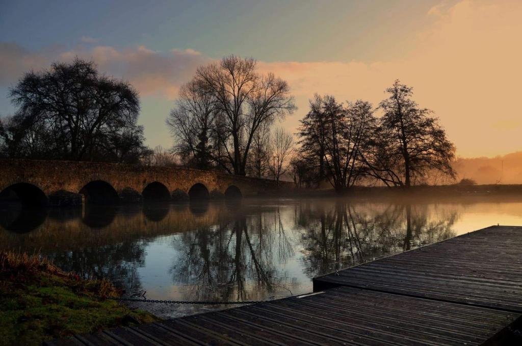 un pont sur une étendue d'eau plantée d'arbres dans l'établissement Maison avec piscine 24heures du Mans, à Yvré-lʼÉvêque