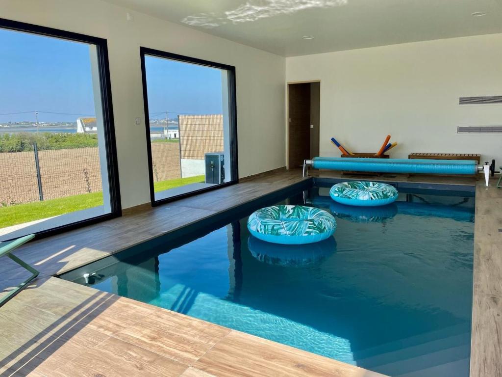 a swimming pool with blue water in a room with windows at Magnifique maison vue mer avec piscine intérieure in Carantec