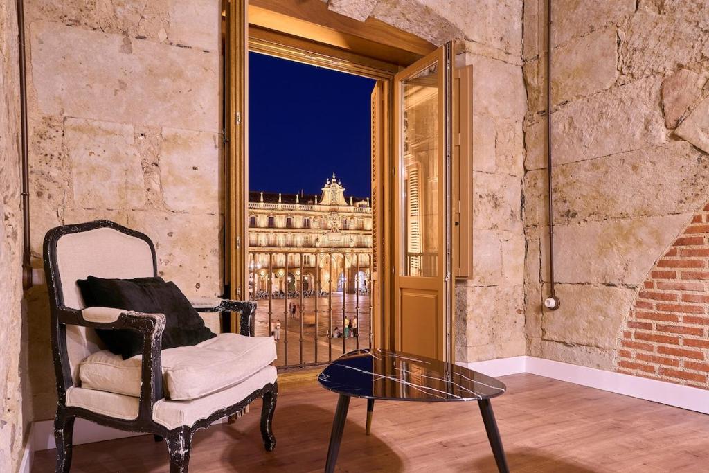 una silla y una mesa en una habitación con ventana en Apartamentos propia Plaza Mayor collection Luxury, en Salamanca