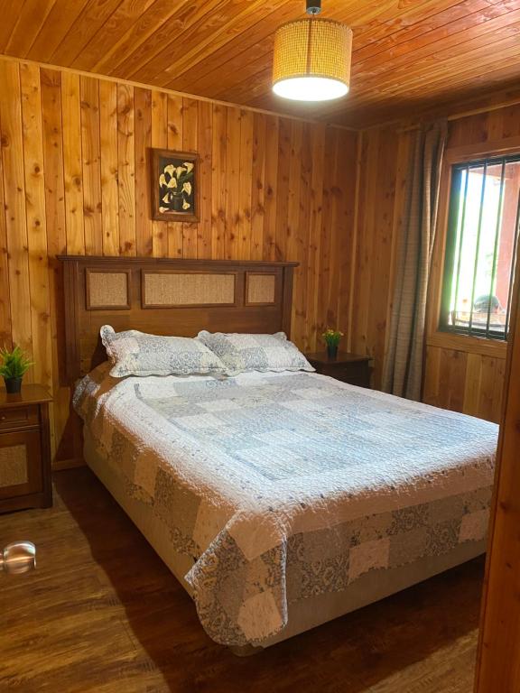 Un dormitorio con una cama en una habitación con paredes de madera. en Cabañas Antualen Casa 2, en Pucón