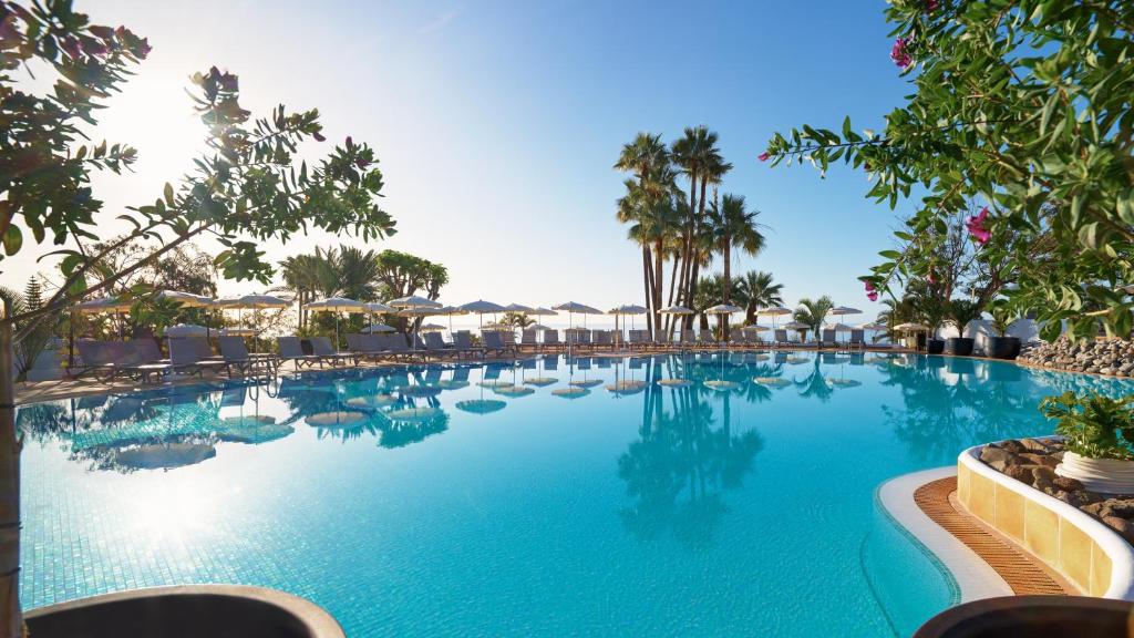 a pool at a resort with palm trees and chairs at Hotel Jardín Tecina in Playa de Santiago