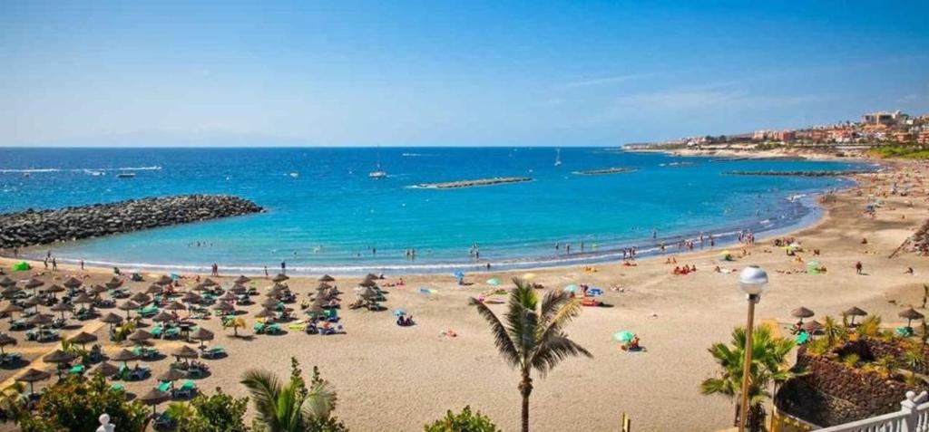 a beach with umbrellas and people in the water at Los Cristianos Penthouse in Arona