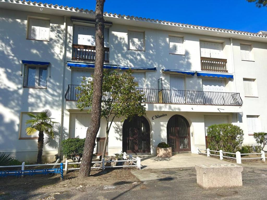 un bâtiment blanc avec un arbre devant lui dans l'établissement Charmant T3 à 50m de la plage, Argelès-sur-Mer - FR-1-388-234, à Argelès-sur-Mer