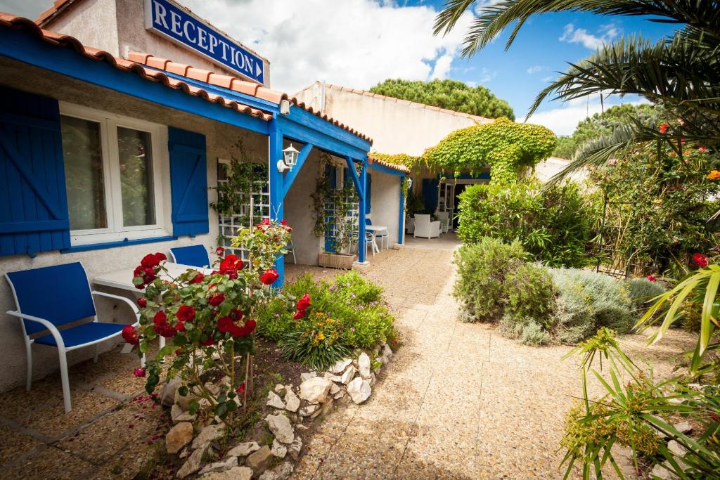 a house with blue trim and flowers in the yard at Hotel Des 4 Vents "Esprit Camargue" Parking Privé Gratuit in Aigues-Mortes