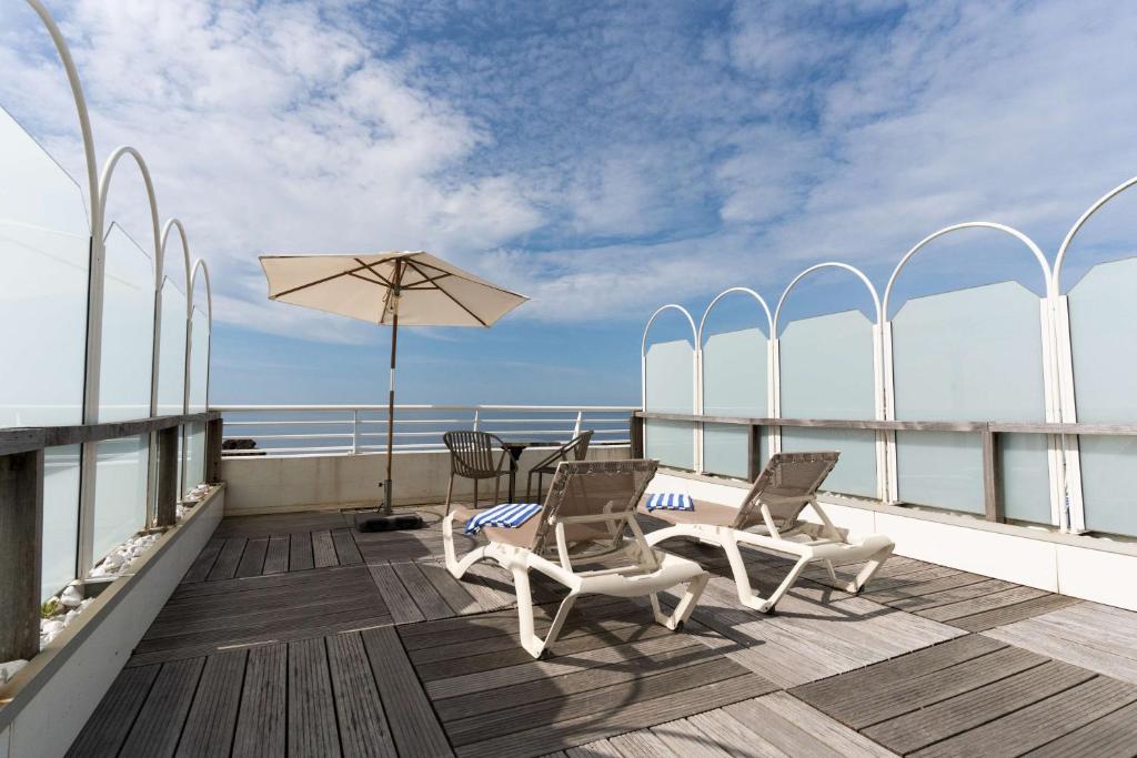 a balcony with chairs and a table and an umbrella at Best Western Hotel De La Plage Saint Marc sur Mer in Saint-Nazaire
