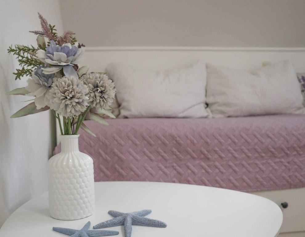 een witte vaas met bloemen op een tafel met een bank bij Ledinić room in Mokošica