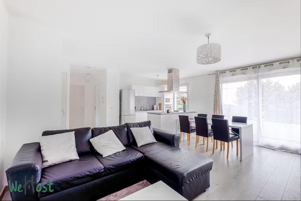 a living room with a black leather couch and a kitchen at Perollier - CI - Lyon 2 - Bedroom apartment with balcony and pool in Écully