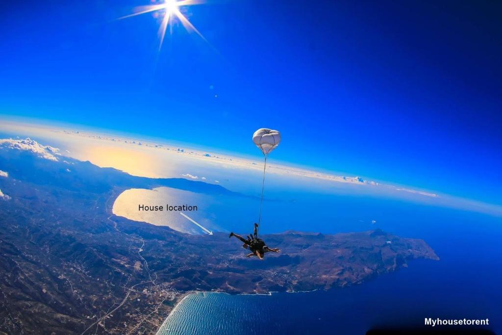 a person is dangling from a hot air balloon over the ocean at House with Private Place To Swim, Solitary, View in Ravdhoúkha