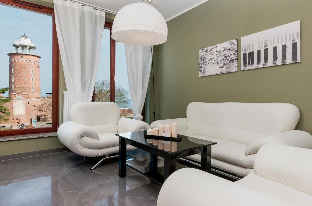 a living room with white chairs and a table and a lighthouse at Jantar Apartamenty Deluxe Sea View in Kołobrzeg