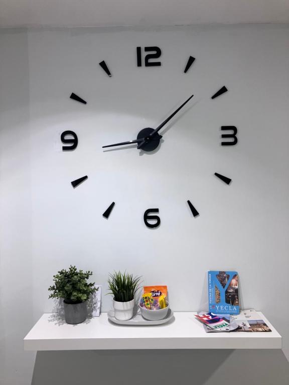 a clock on a white wall with plants on a table at Alojamientos centro in Yecla
