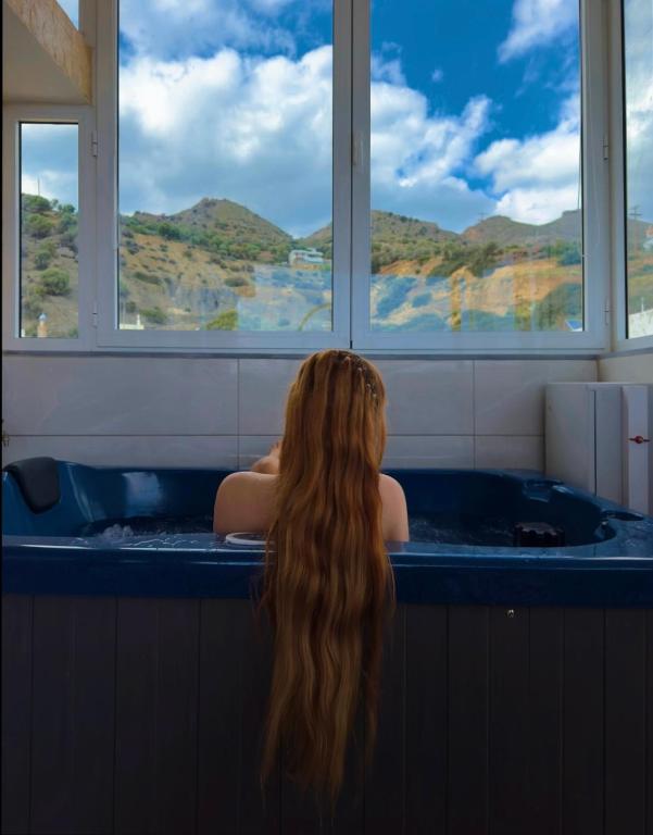 a woman sitting in a bath tub looking out the window at Filocsenia luxury suite in Tsoutsouros