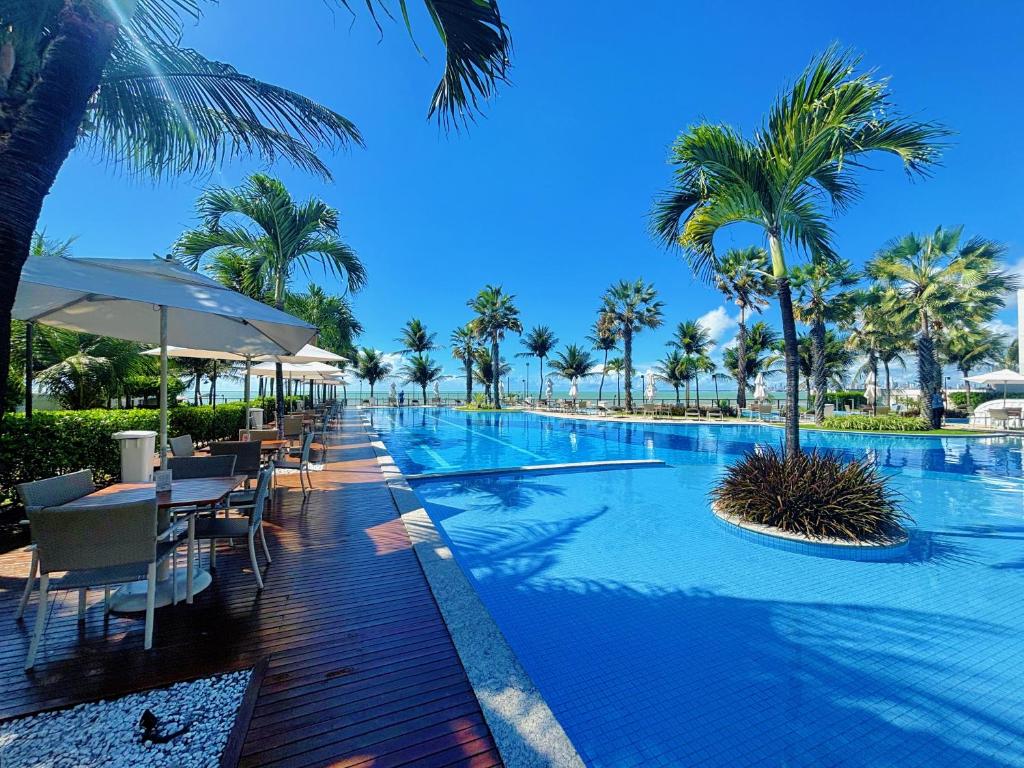 a swimming pool with tables and chairs and palm trees at Viva o Paraíso – Condomínio Exclusivo Beira-Mar e Lazer Completo in Ilha da Restinga