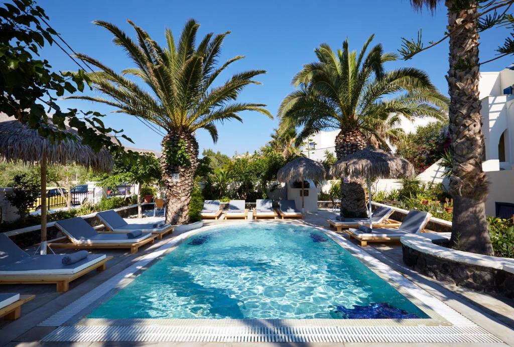 a pool with chaise lounge chairs and palm trees at Hermes Hotel in Kamari