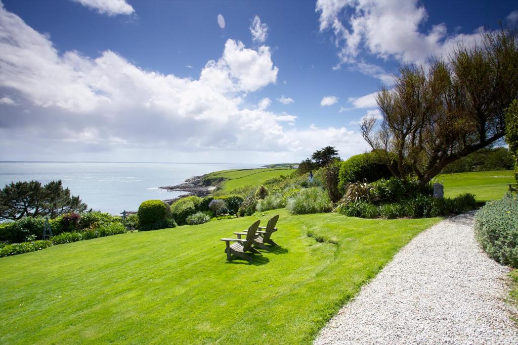 two benches sitting on a grassy hill overlooking the ocean at Driftwood in Porthscatho