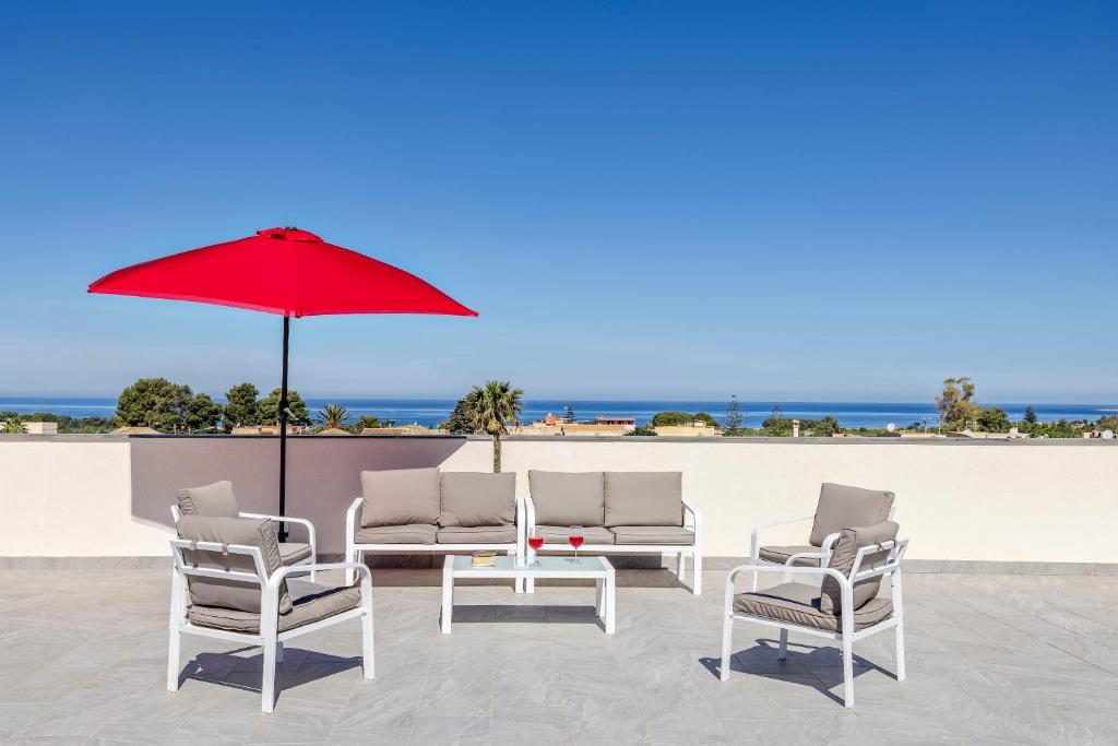 a group of chairs and a table with a red umbrella at Case Vacanza Loria in Castelluzzo