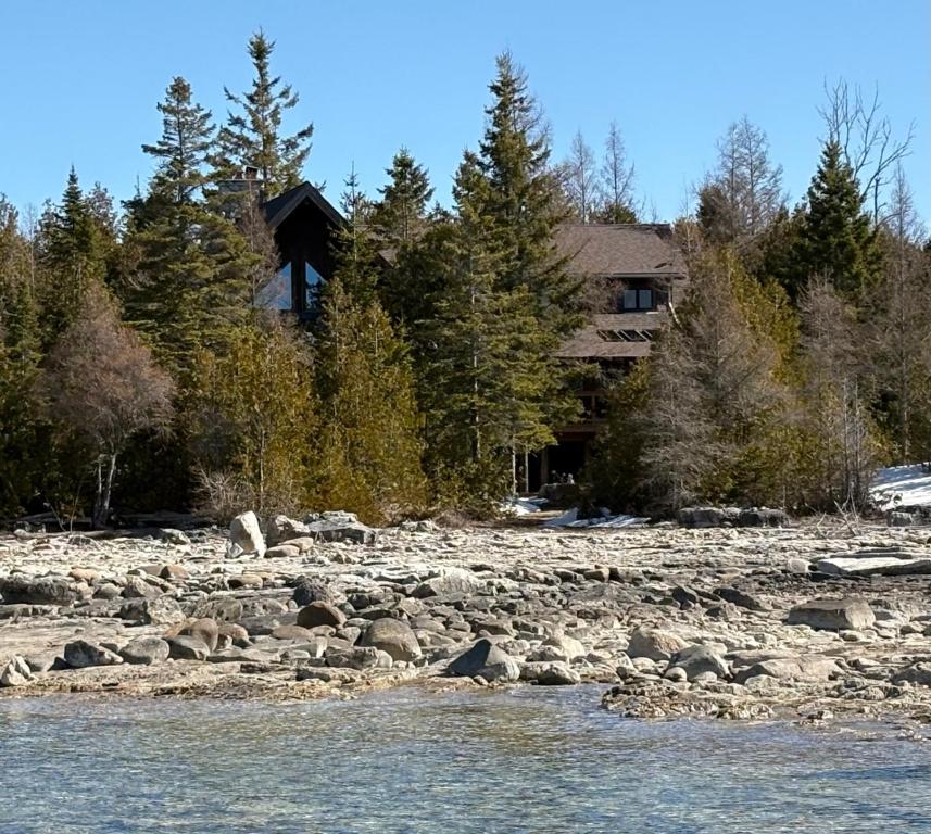 a house on the side of a rocky river at Massive Rustic Waterfront Log Cabin in Stokes Bay