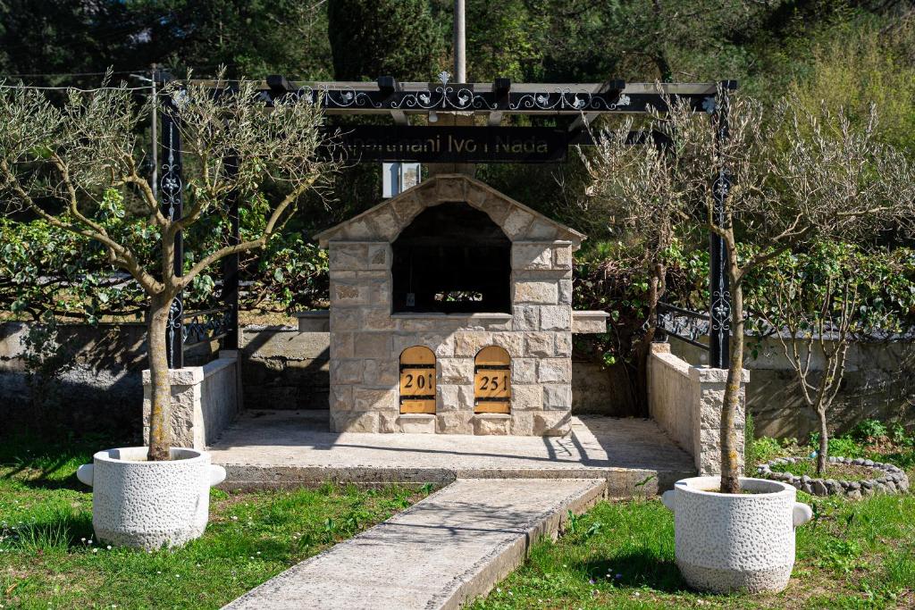 a stone fireplace with two trees in a yard at Apartments Ivo Bozinovic in Tivat