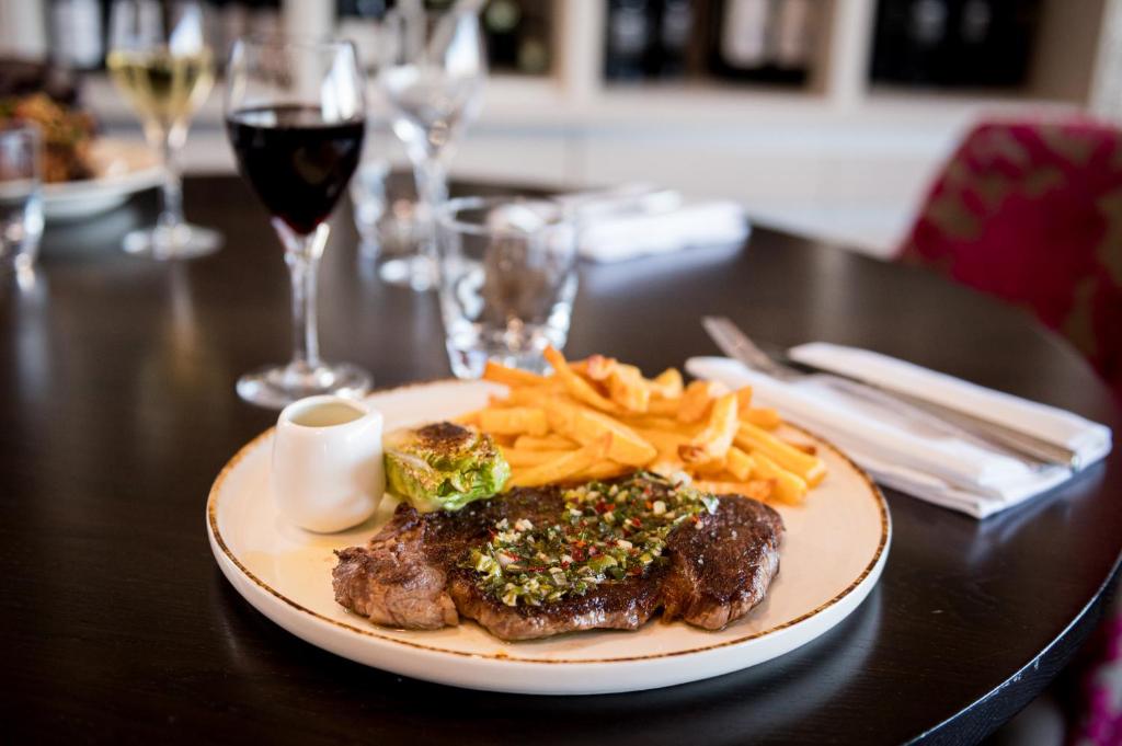 a plate of steak and fries on a table with wine at Saint Aubin Logis Hôtel & Restaurant in Saint-Aubin-sur-Mer