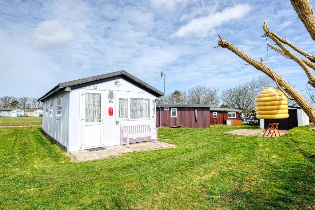 a small white shed with a bench in a yard at Two Hoots Chalet in Mundesley