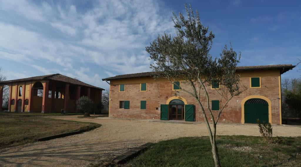 um velho edifício de tijolos com portas verdes e uma árvore em La Barchessa Country House em Budrio