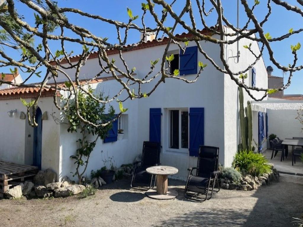 une maison blanche avec des portes bleues, une table et des chaises dans l'établissement Maison confortable à Barbâtre, près de la plage - FR-1-823-148, à Barbâtre