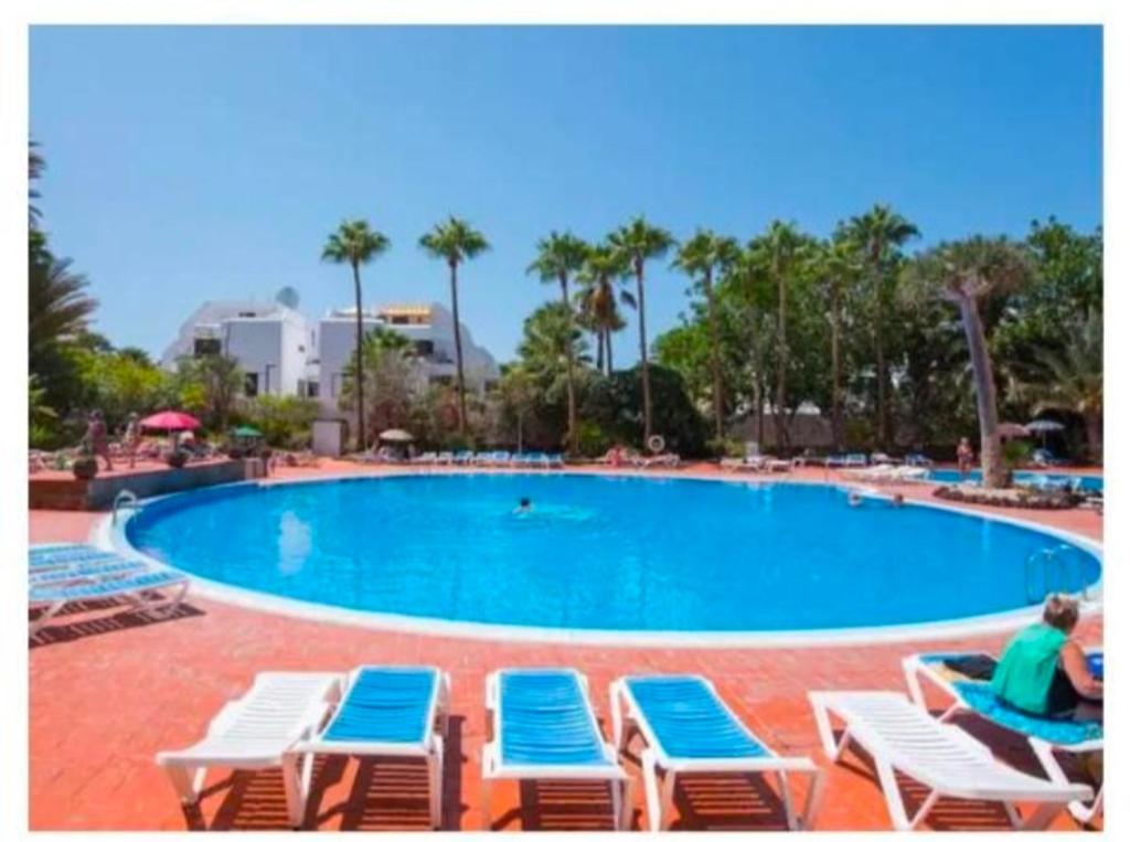 a woman sitting on lounge chairs next to a swimming pool at Eldorado MILE STUDIO in Playa de las Americas