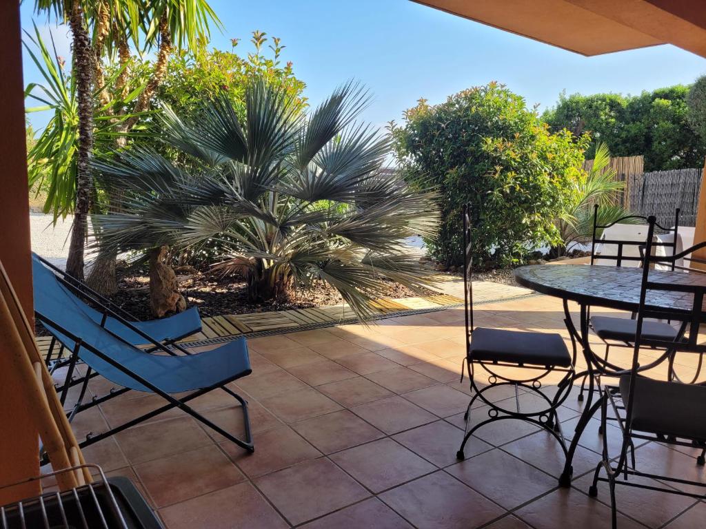 un patio avec une table, des chaises et un palmier dans l'établissement Giens-T2 charme-7m à pied plage - Rez de jardin, à Hyères