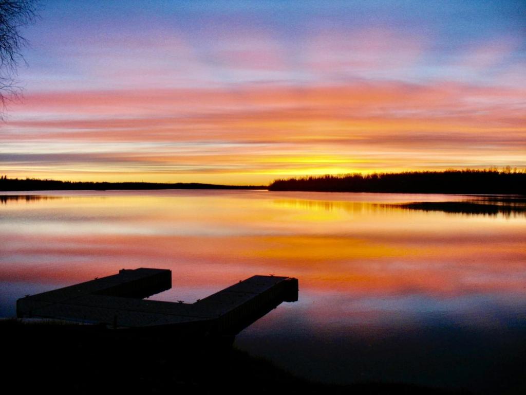 a sunset on a lake with a boat in the water at Downtown Wasilla Lakefront Home in Wasilla