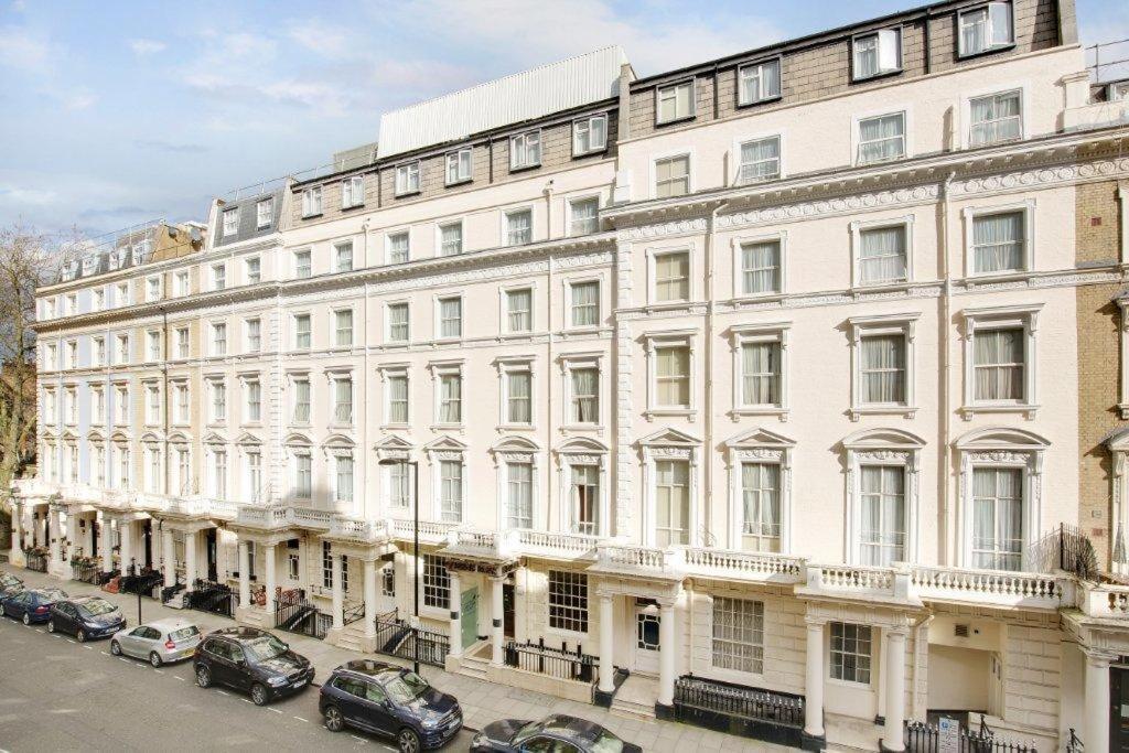 un gran edificio blanco con coches estacionados frente a él en Queens Park Hotel, en Londres