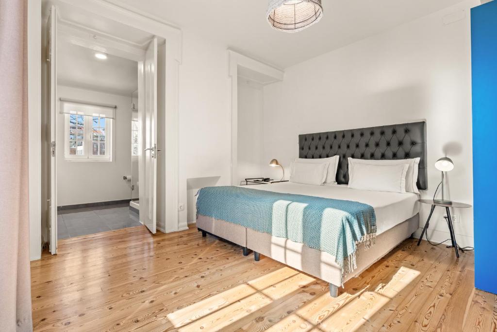 A sunlit bedroom with a tufted headboard, wooden floor and adjoining doorway.