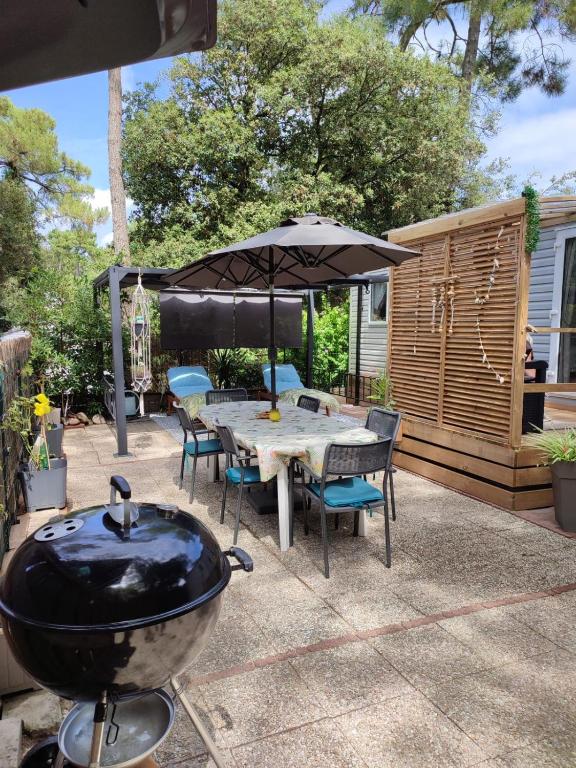 - un barbecue et une table avec des chaises et un parasol dans l'établissement MH Les Mimosas sur terrain privé en pinède La Tranche Sur Mer, à La Tranche-sur-Mer