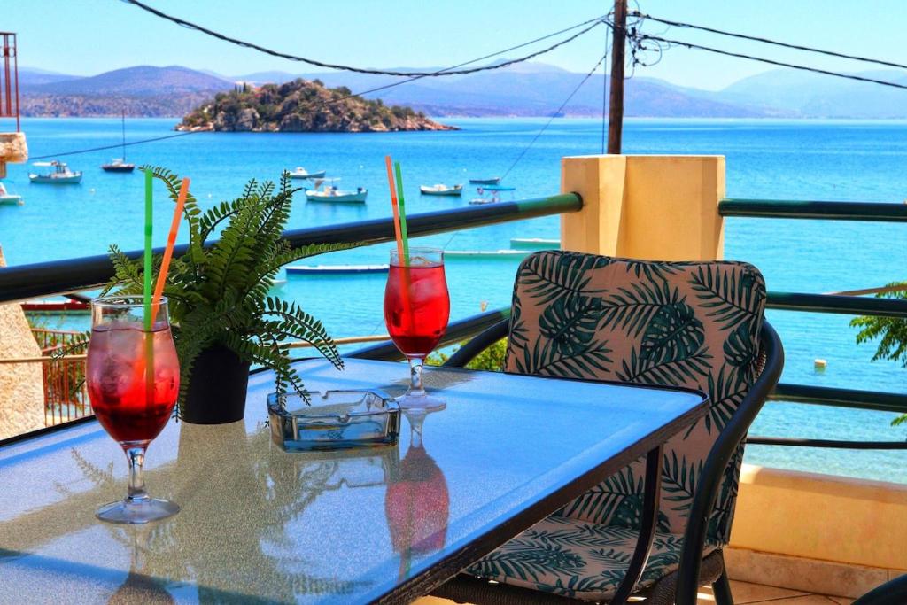 a table with two glasses on a balcony with a view of the water at Eleni's Summer Apartment in Tolo