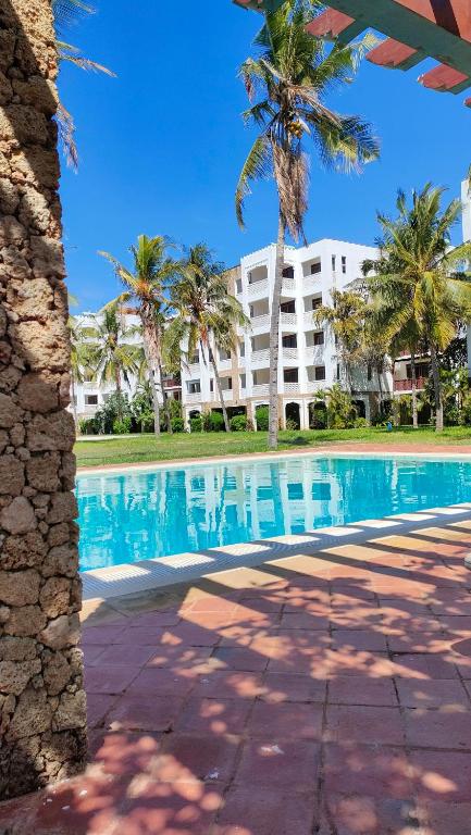 a swimming pool with palm trees in front of a building at Sultan Palace in Mombasa