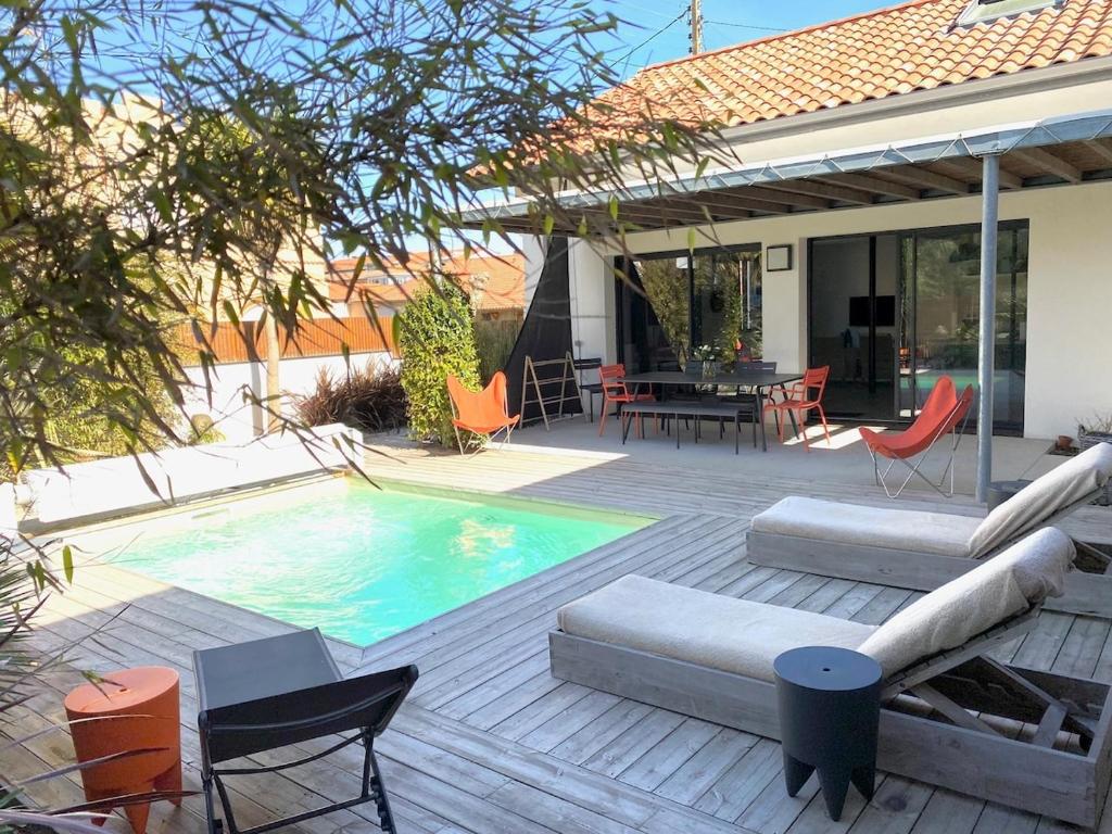 une terrasse avec une piscine, une table et des chaises dans l'établissement Villa classée 5 étoiles 200m de la plage piscine chauffée 5 vélos, à Capbreton