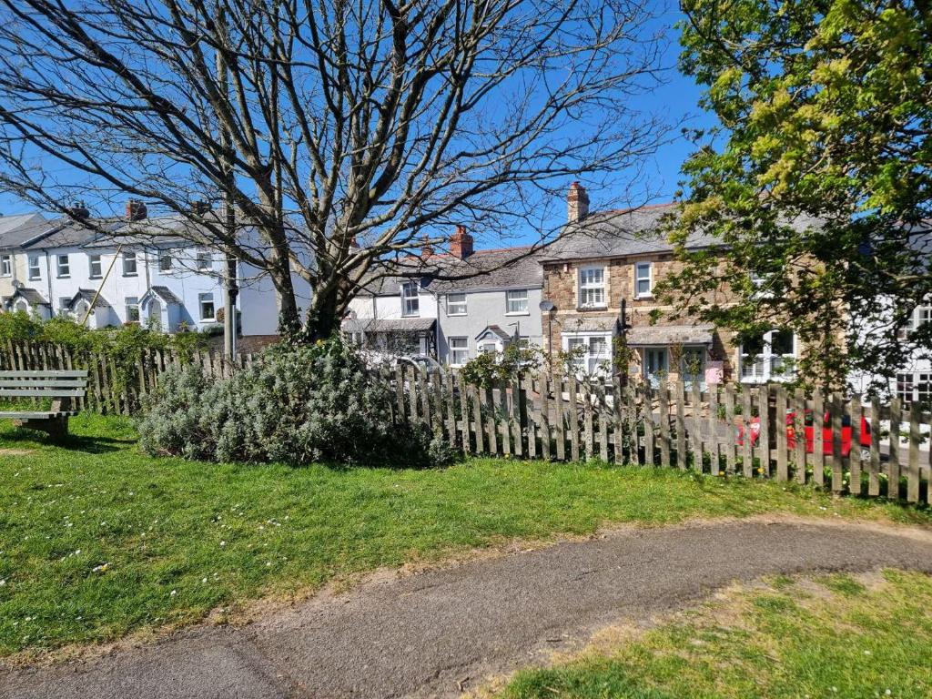 a fence in front of a house with a tree at Cosy Cottage in a quaint village in North Devon. in Abbotsham