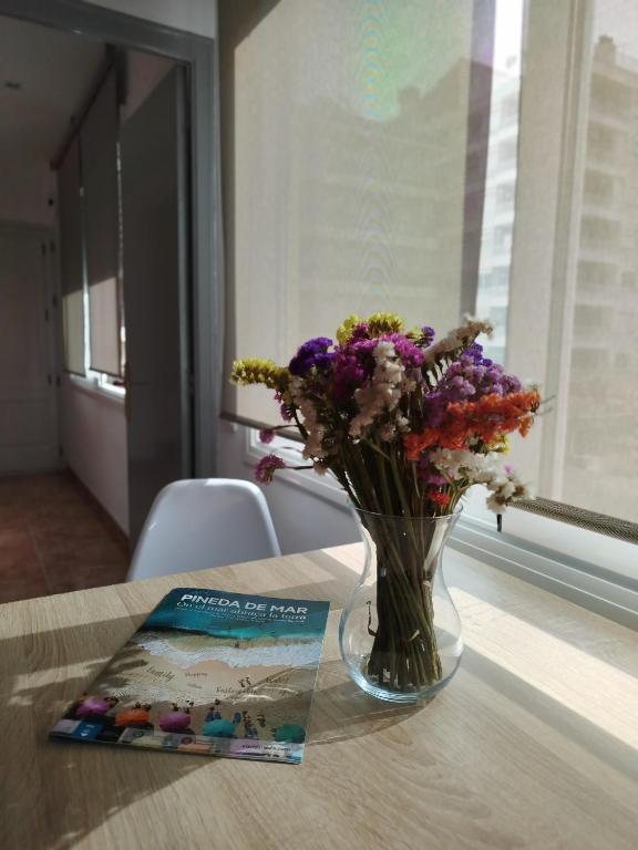 a vase of flowers next to a book on a table at Mar & Sol Pineda in Pineda de Mar