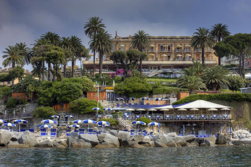 a beach with palm trees and umbrellas overlooking a body of water at Hotel Continental in Santa Margherita Ligure