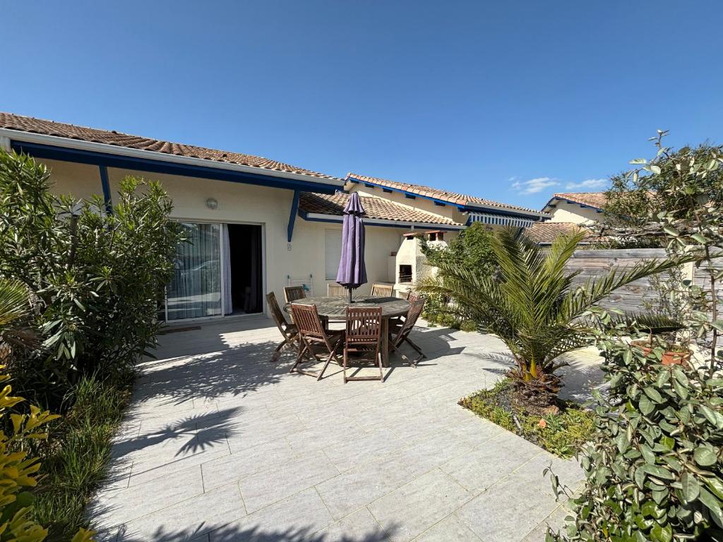 un patio avec une table, des chaises et un parasol dans l'établissement Maison en Duplex au Pied des Dunes à Biscarrosse - Calme et Confort, Parking et Terrasse - FR-1-319-183, à Biscarrosse-Plage