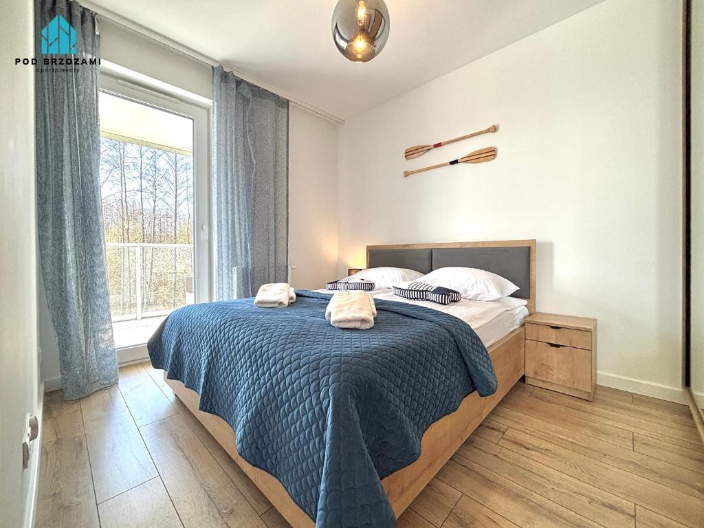 a bedroom with a bed with a blue blanket and a window at Pod Brzozami Apartamenty Gąski in Gąski