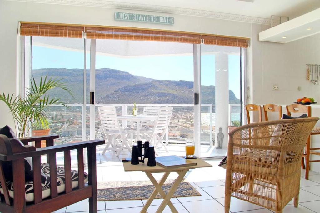 Una sala de estar con una mesa y sillas y una gran ventana. en Crow's Nest Fish Hoek Apartment, en Fish Hoek