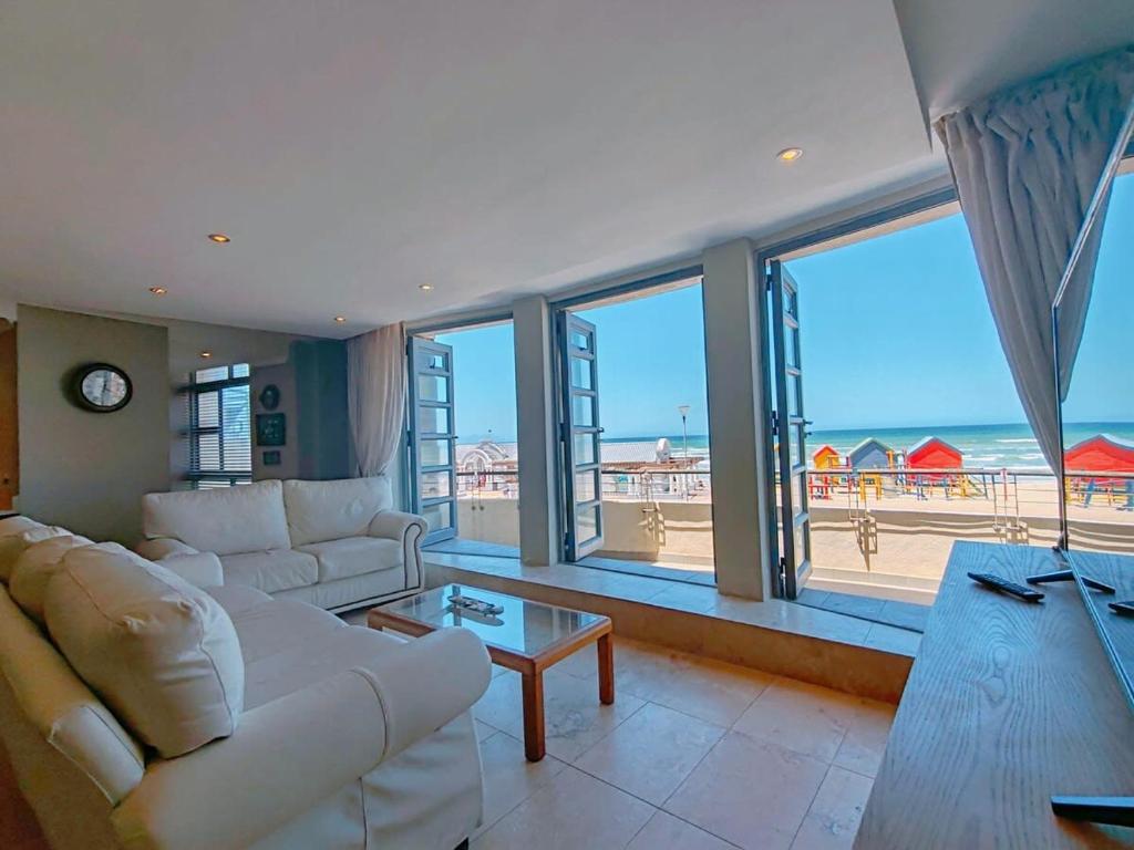 a living room with a white couch and a view of the ocean at Sunrise Deck Empire Apartment in Muizenberg